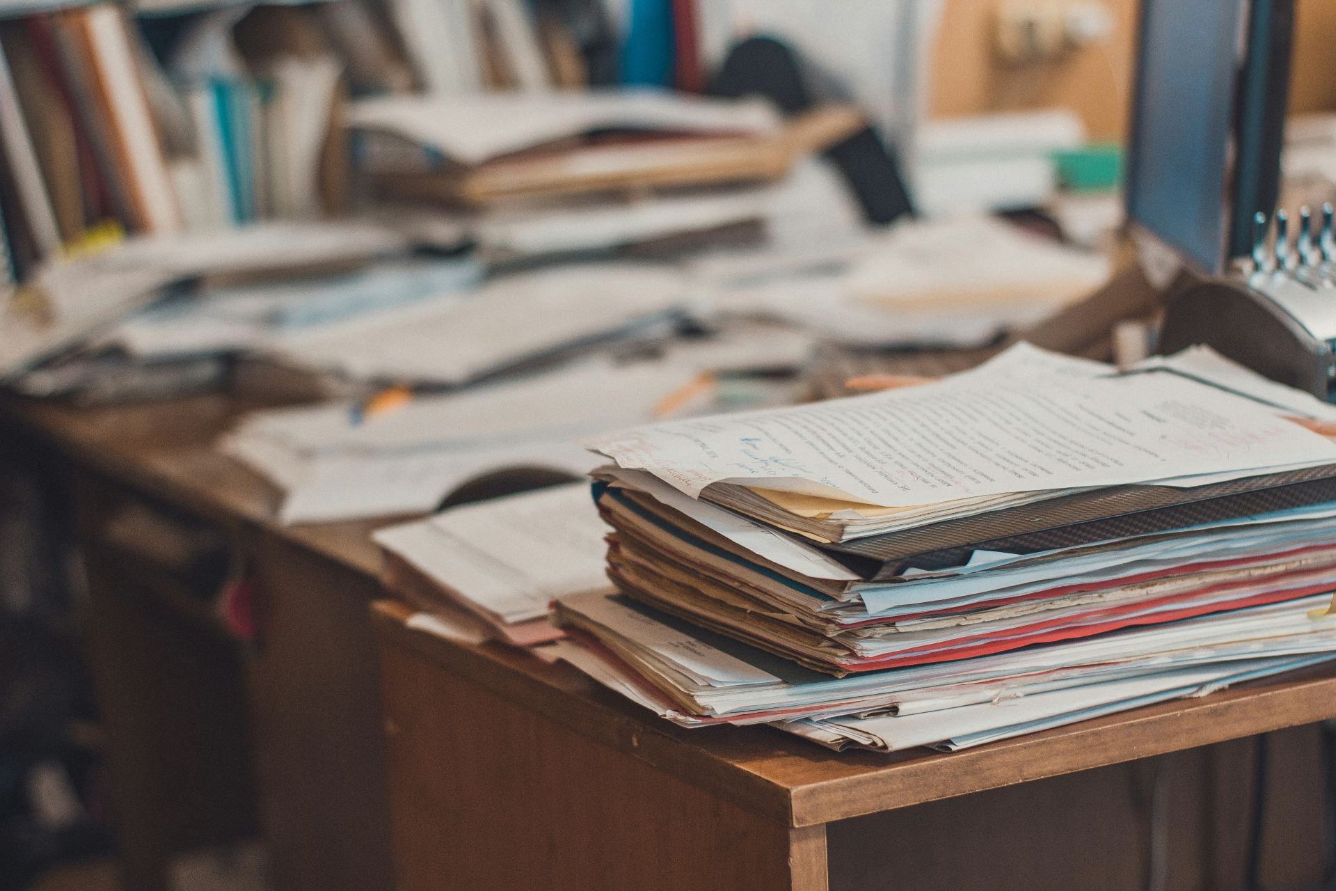 A chaotic stack of paper manuals, receipts, and notes on a cluttered desk